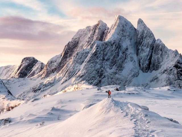 Man with backpack standing on snowy mountain peak during sunset