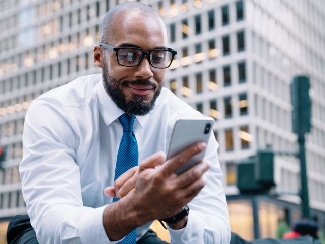 Black professional looking at his phone and smiling in the city