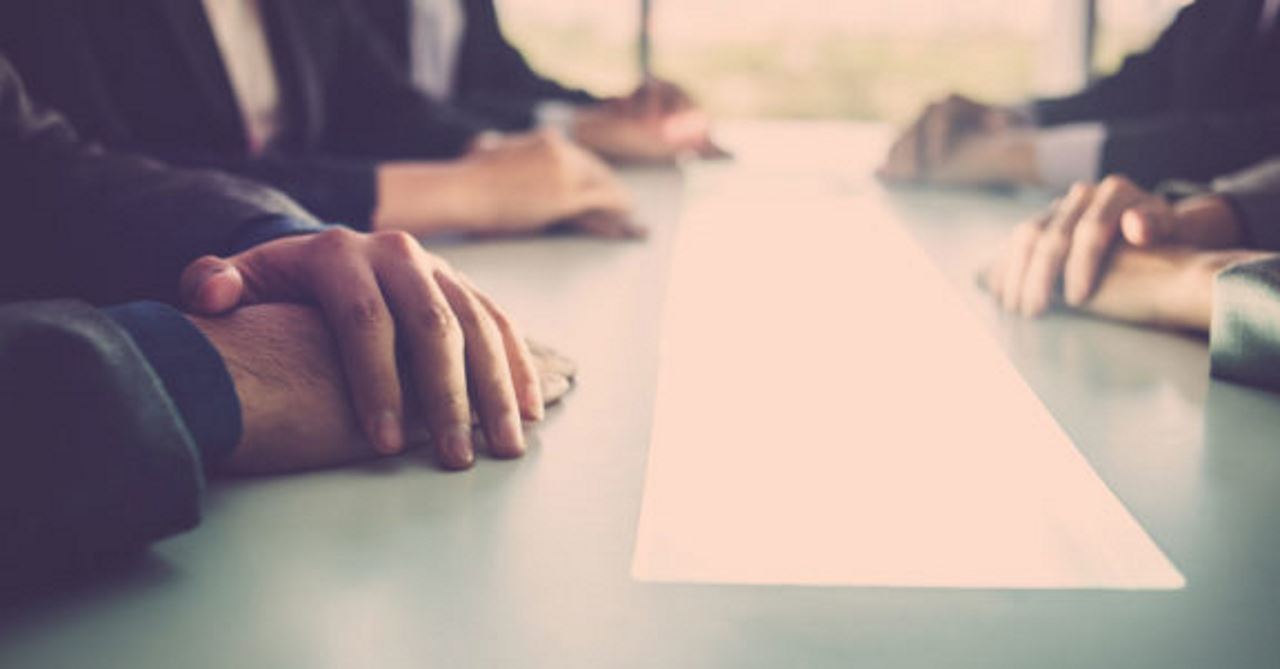 group of employees sitting across from each other at a conference table with their hands on the table in front of them