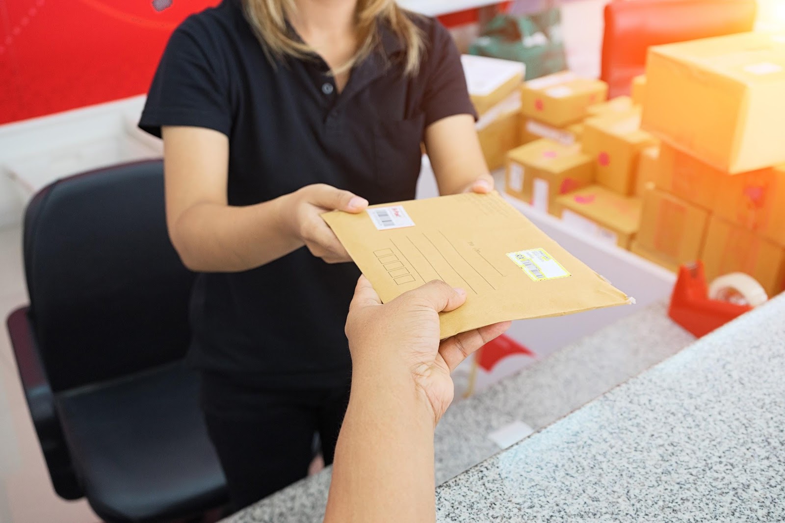 hand passing an envelope across the counter to a woman at a post office