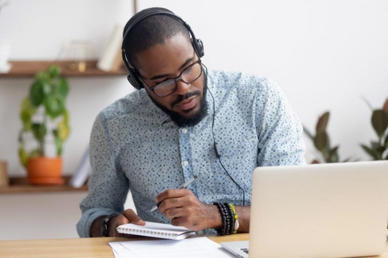 man at desk doing virtual onboarding on laptop and taking notes