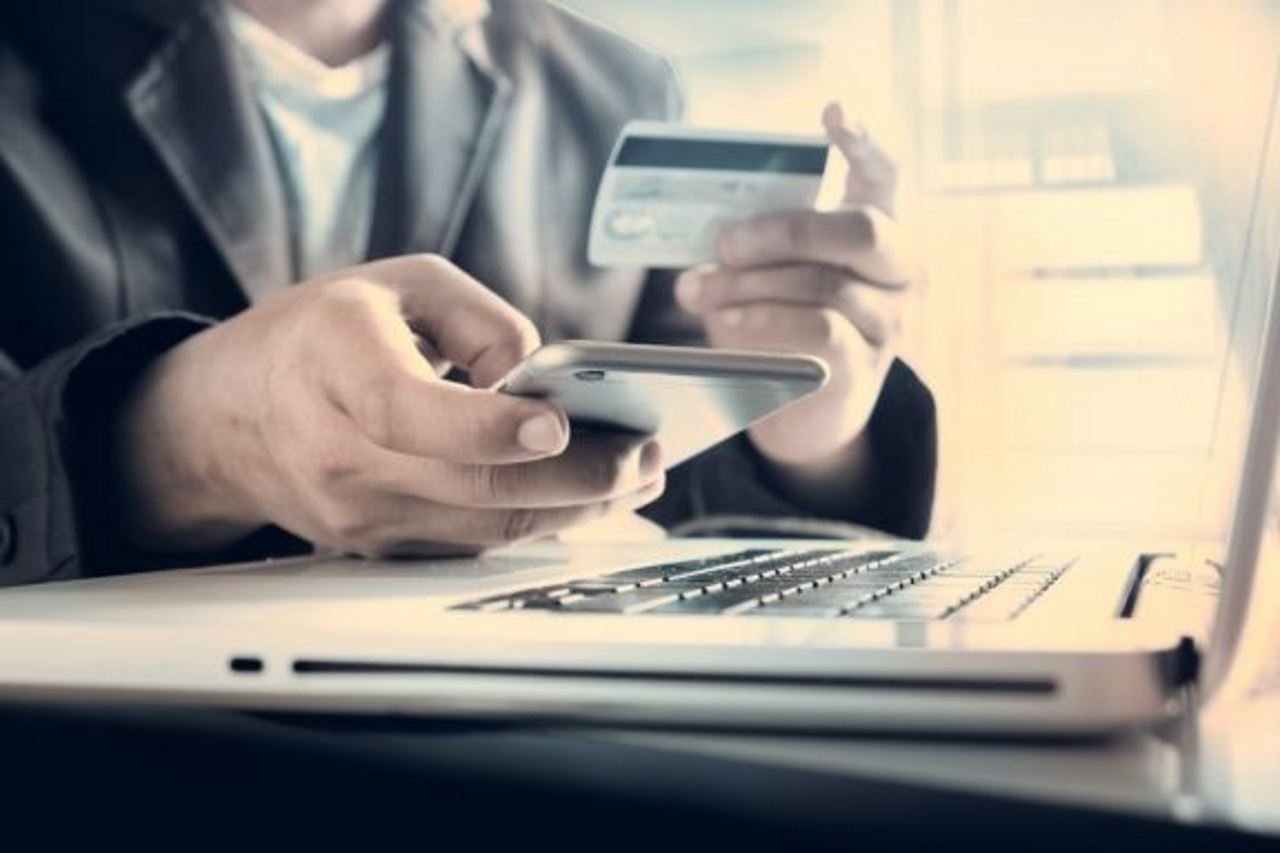 man's hand holding phone in one hand and credit card in the other hand in front of laptop