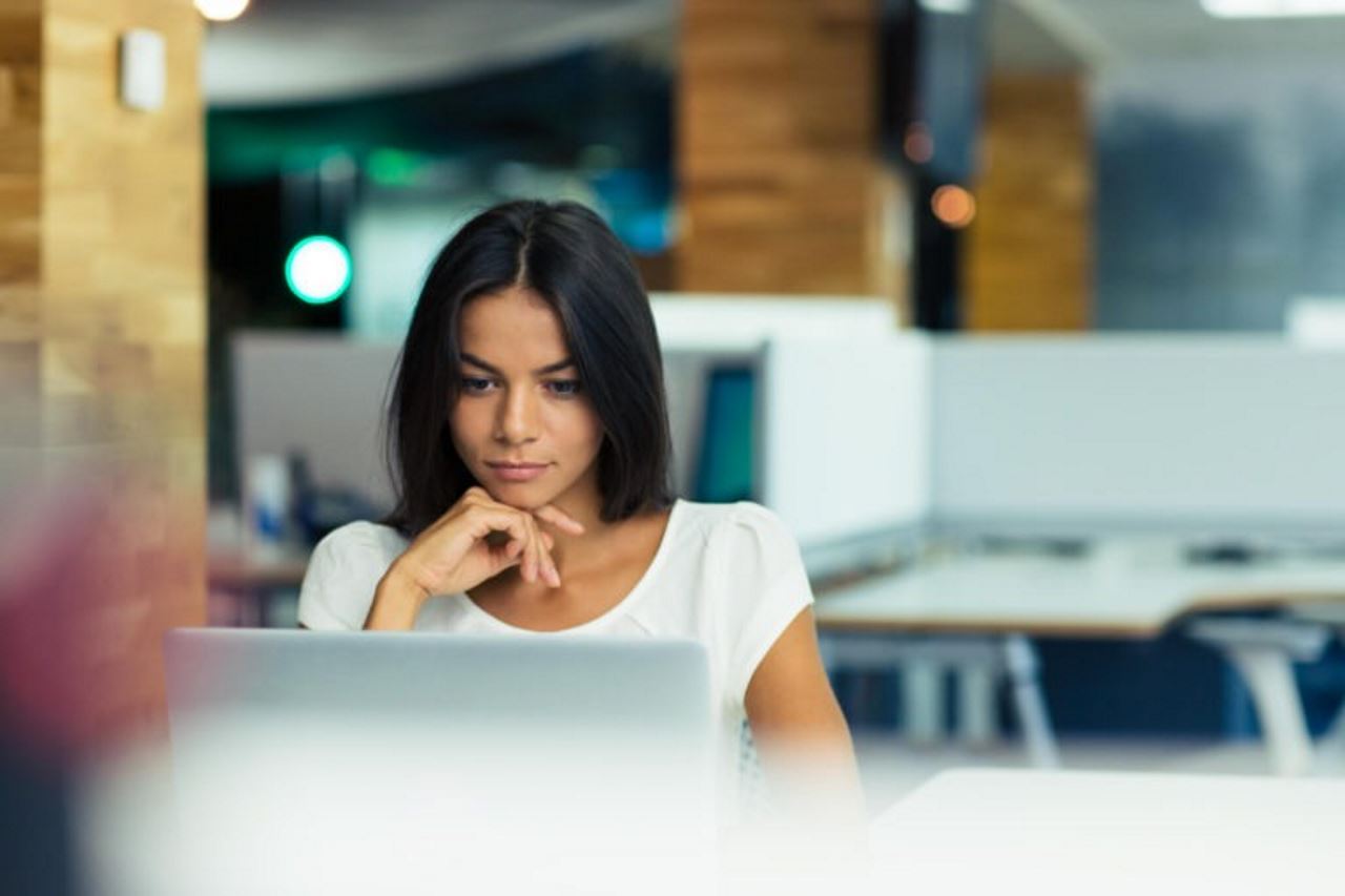 woman sitting at a desk in an office looking at a laptop screen