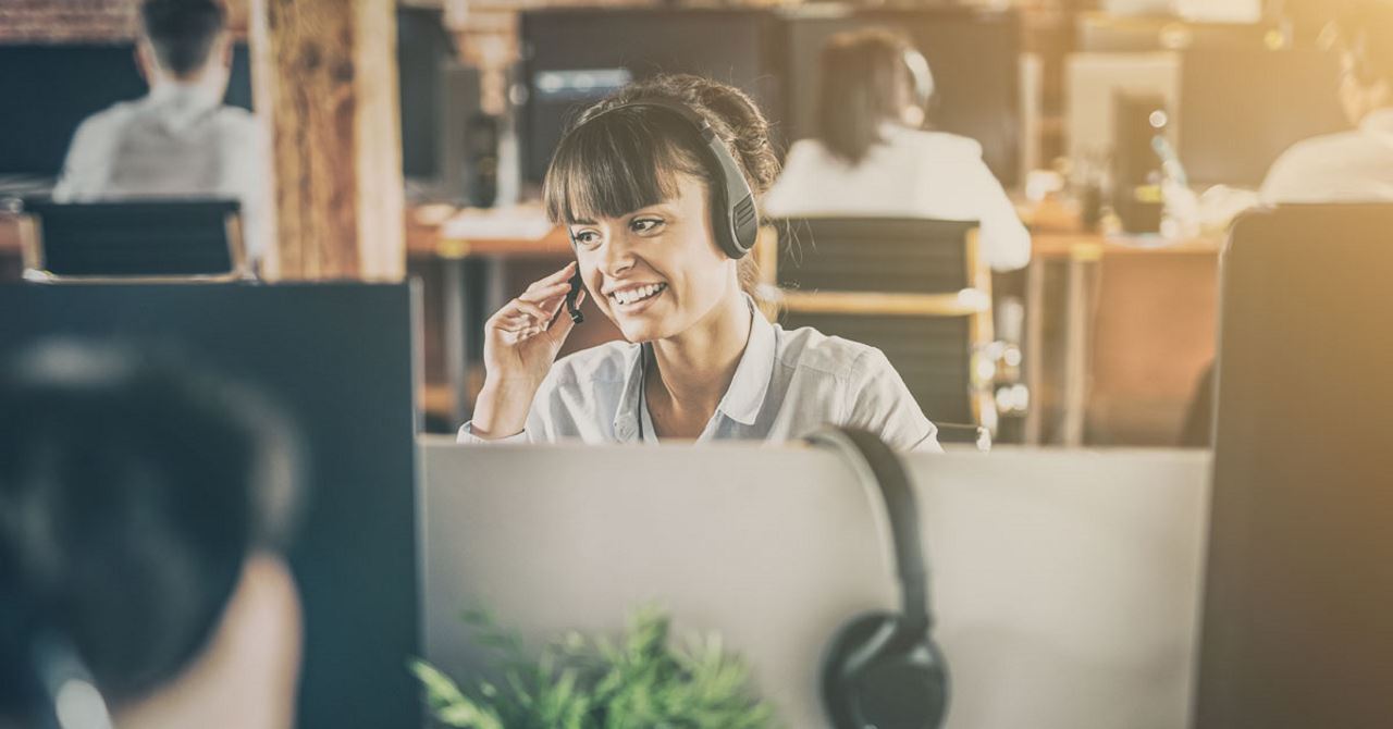 woman sitting at desk in an office with a headset on talking to customers